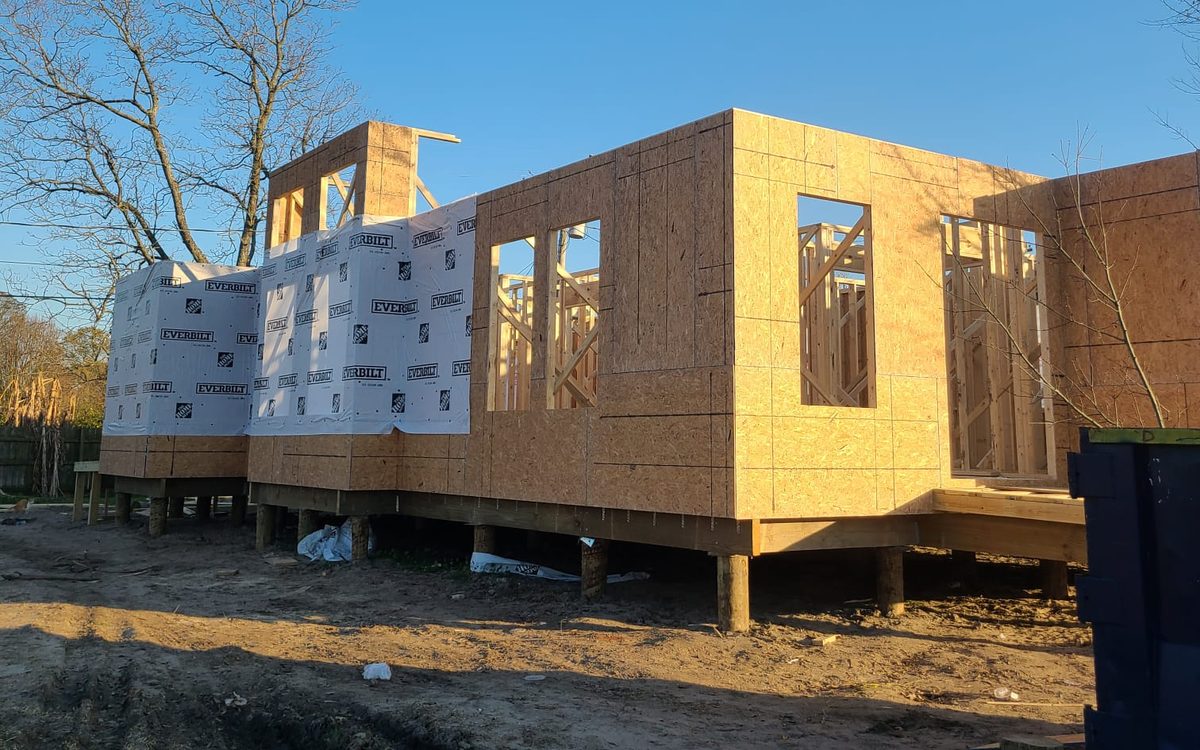 Elevated new home on timber pilings with OSB sheathing and house wrap under a clear blue sky