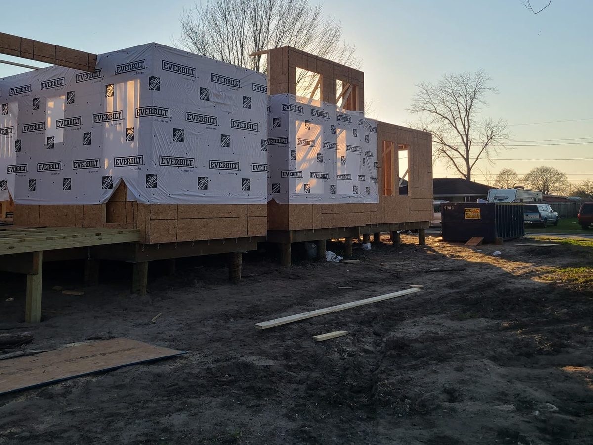 Raised new home wrapped in weather barrier at sunset, with framed upper walls