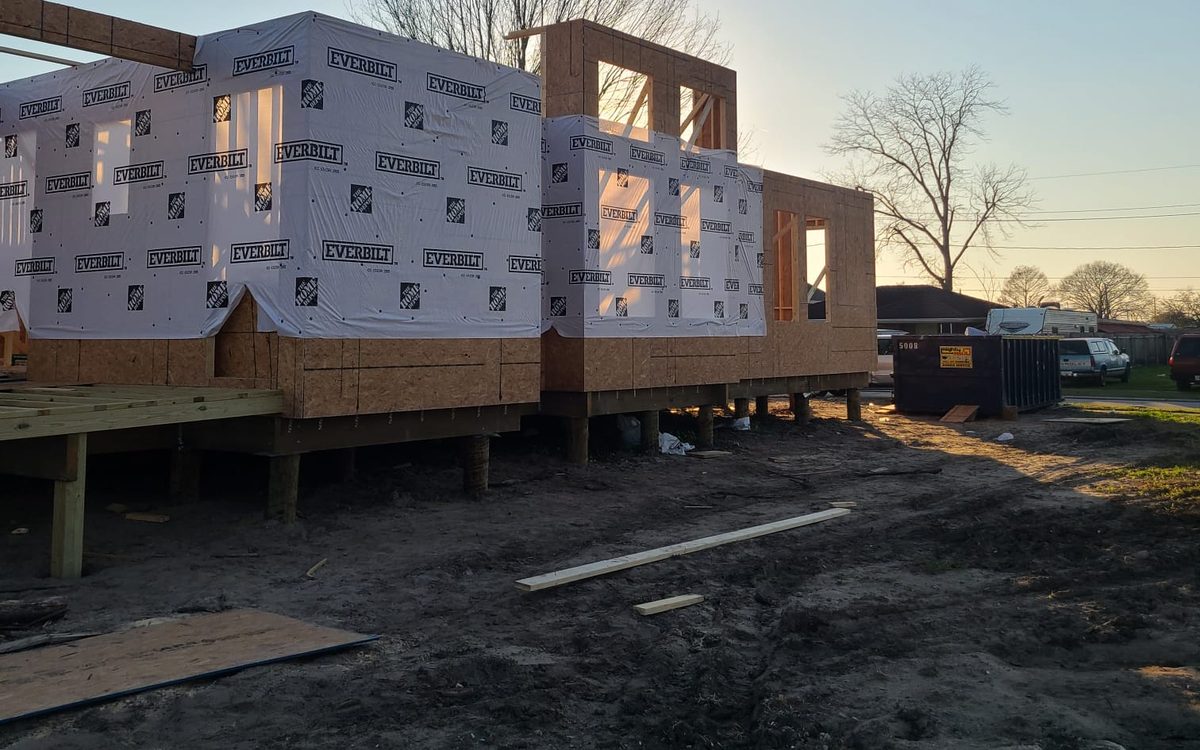 Raised new home wrapped in weather barrier at sunset, with framed upper walls