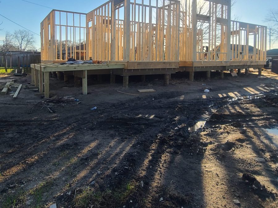 Wall framing on a raised platform supported by timber pilings, backlit by the sun