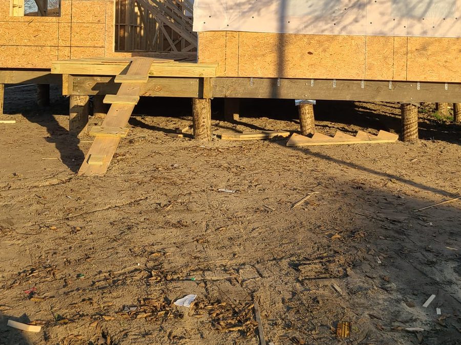 Timber pilings and floor framing beneath an elevated home, with temporary stairs