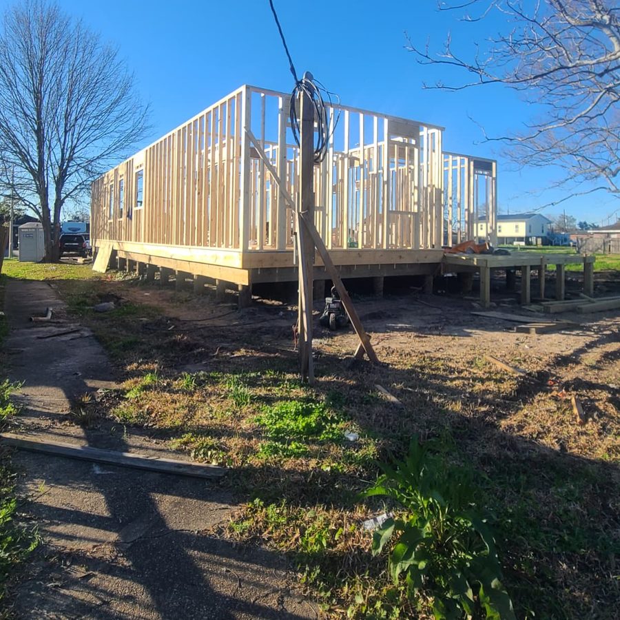 Long house frame standing on a raised floor platform beside a temporary utility pole