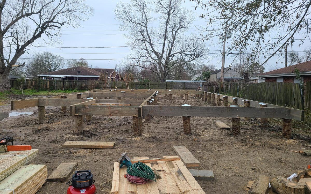 Treated timber pilings and beams set for a pier-and-beam foundation, with lumber and tools in front