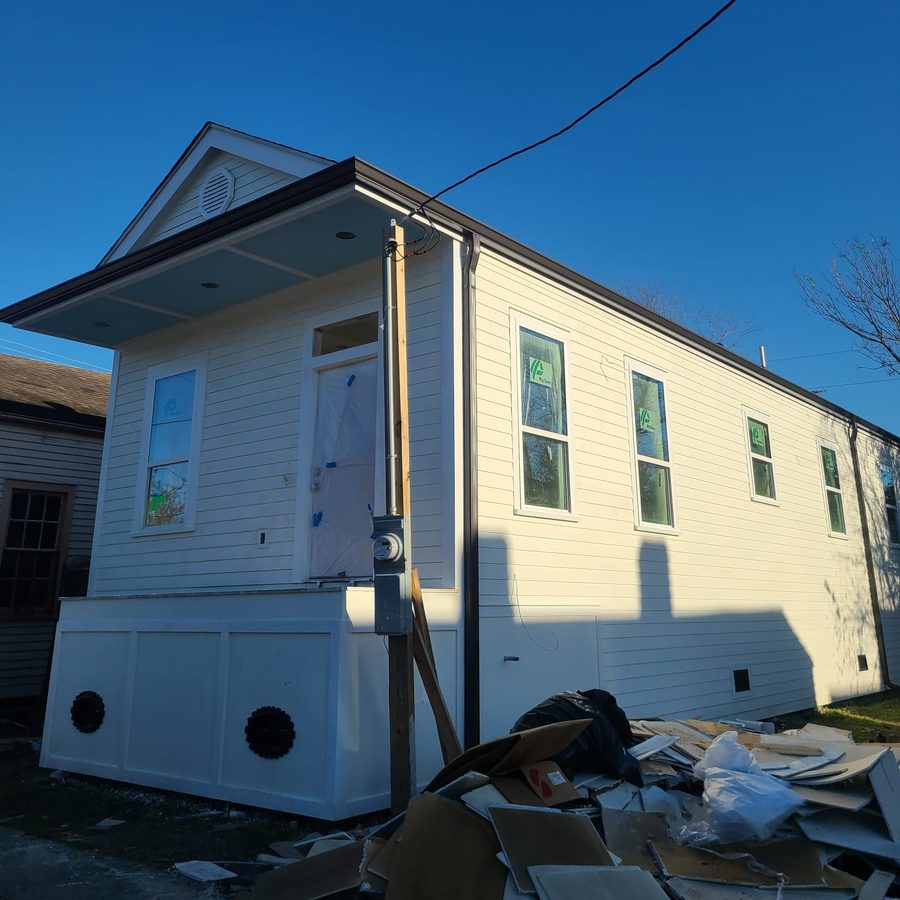 Completed white shotgun-style home with lap siding, gutters and a raised paneled base