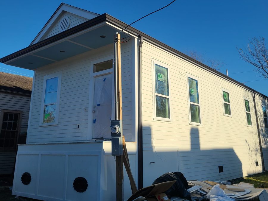 Completed white shotgun-style home with lap siding, gutters and a raised paneled base