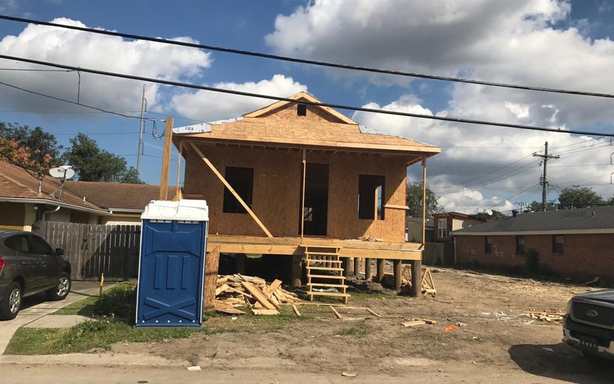 Small raised home sheathed in OSB with a framed porch and temporary stairs