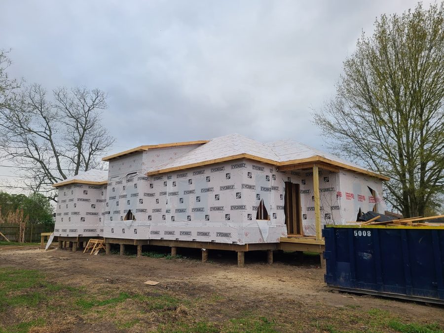 Raised home in house wrap with roof decking installed and porch posts in place
