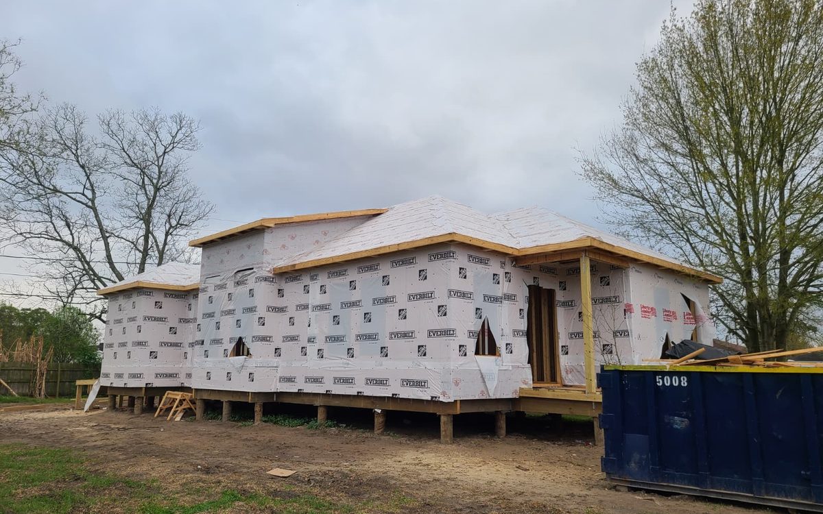 Raised home in house wrap with roof decking installed and porch posts in place