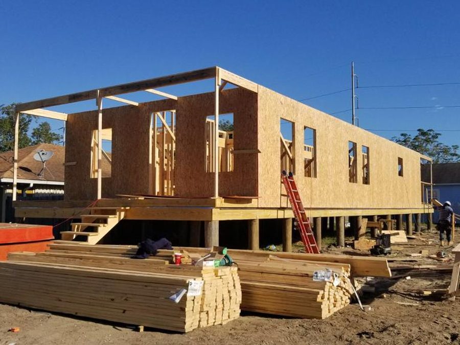 Raised home sheathed in OSB on pilings, with a ladder and lumber on site
