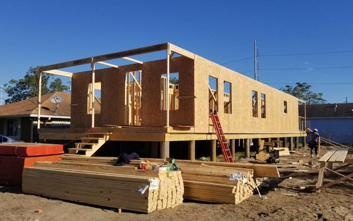 Raised home sheathed in OSB on pilings, with a ladder and lumber on site