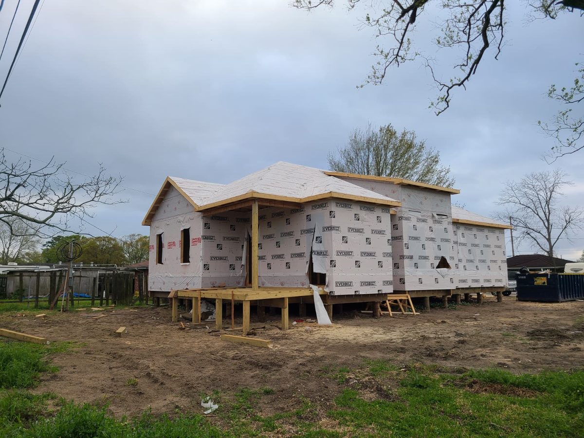 Raised home in house wrap with a hip roof and covered front porch under construction