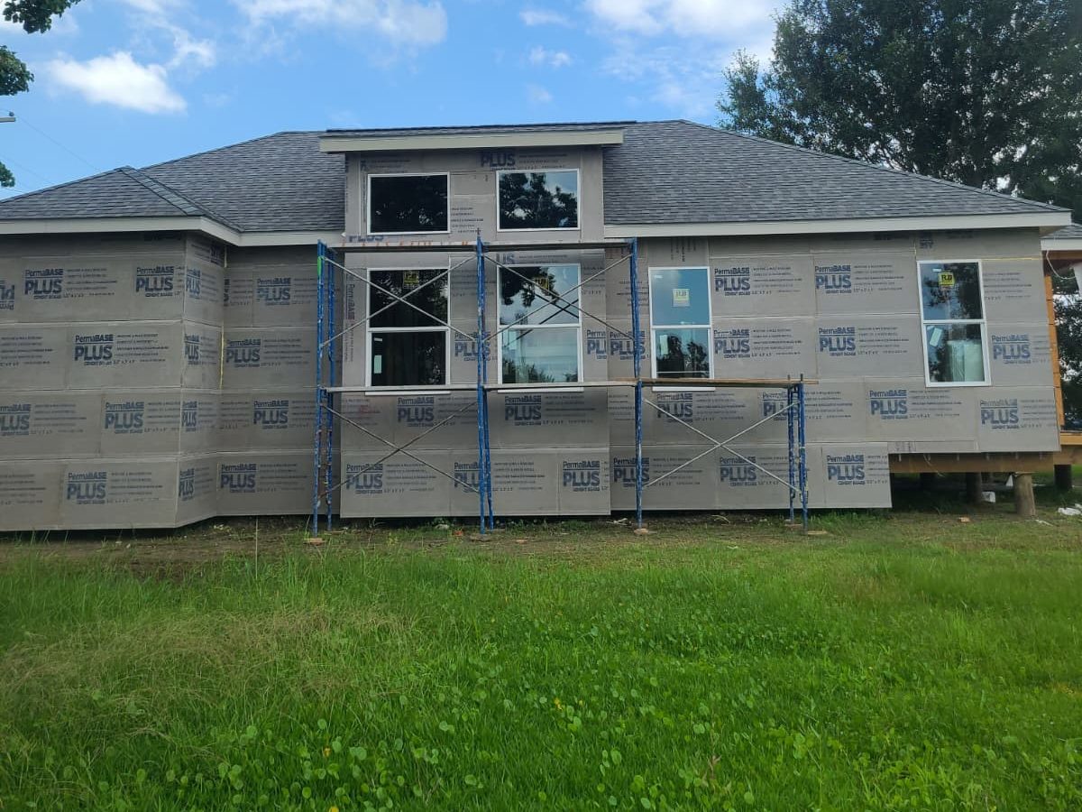 Home clad in cement board with a new shingle roof and scaffolding at the front