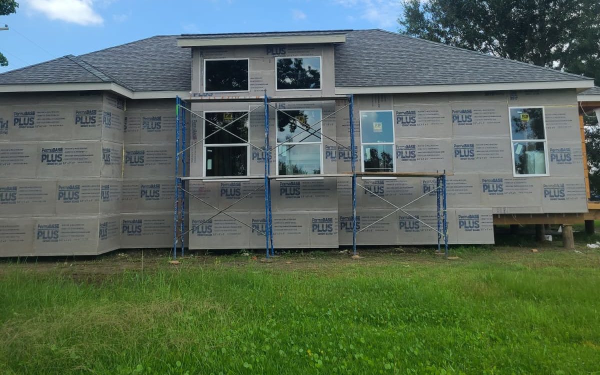 Home clad in cement board with a new shingle roof and scaffolding at the front