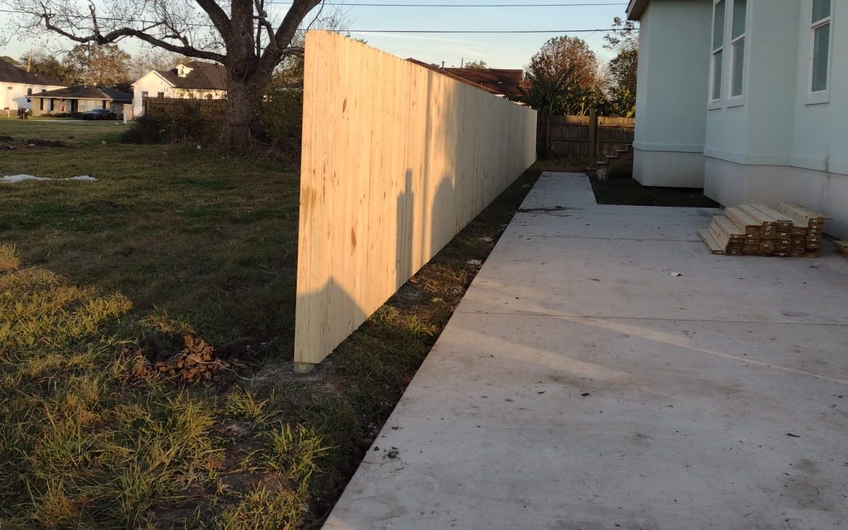 New concrete driveway running along a home beside a new wood privacy fence