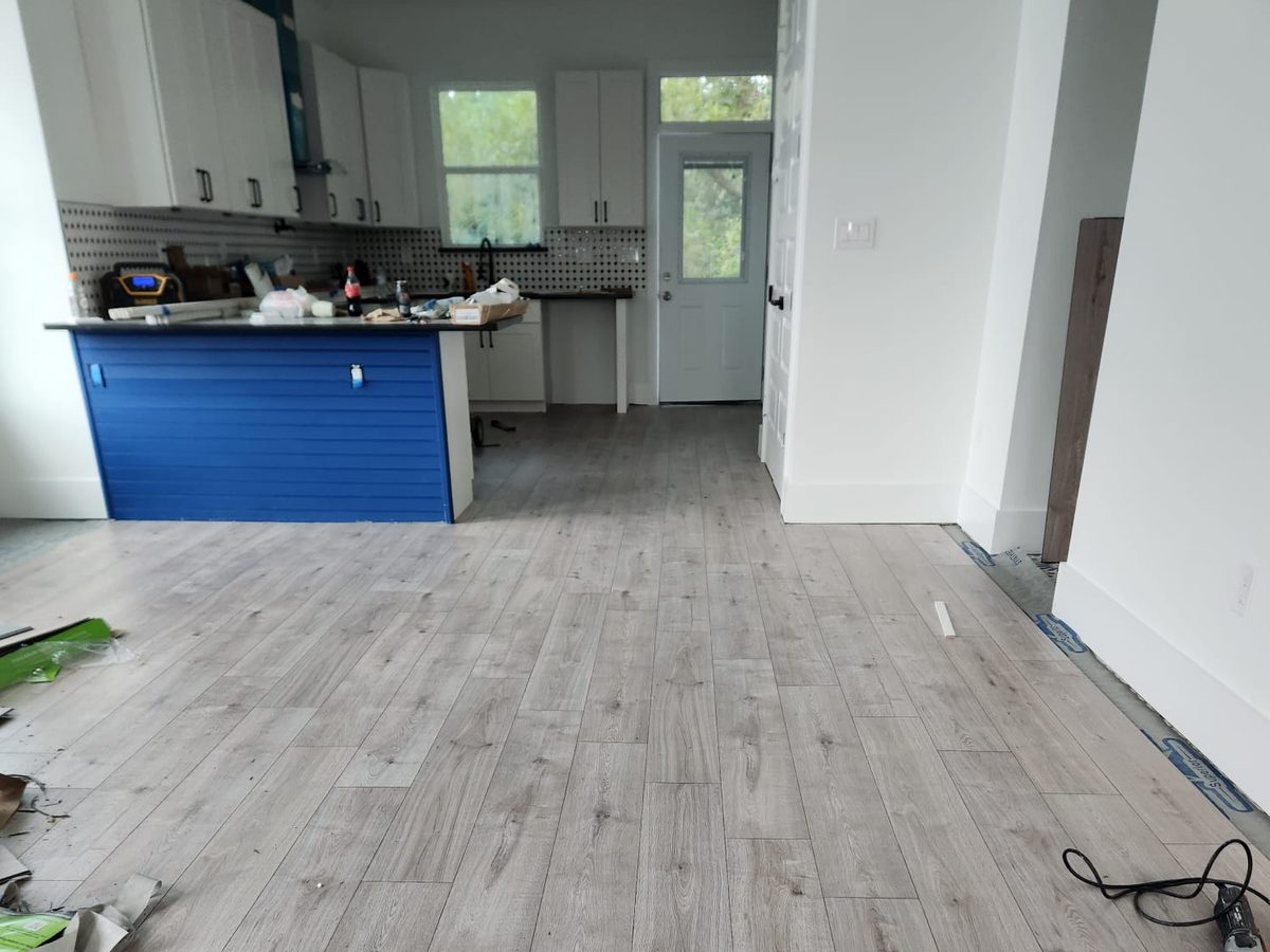 Kitchen with white shaker cabinets, patterned backsplash and a blue island, with new plank flooring