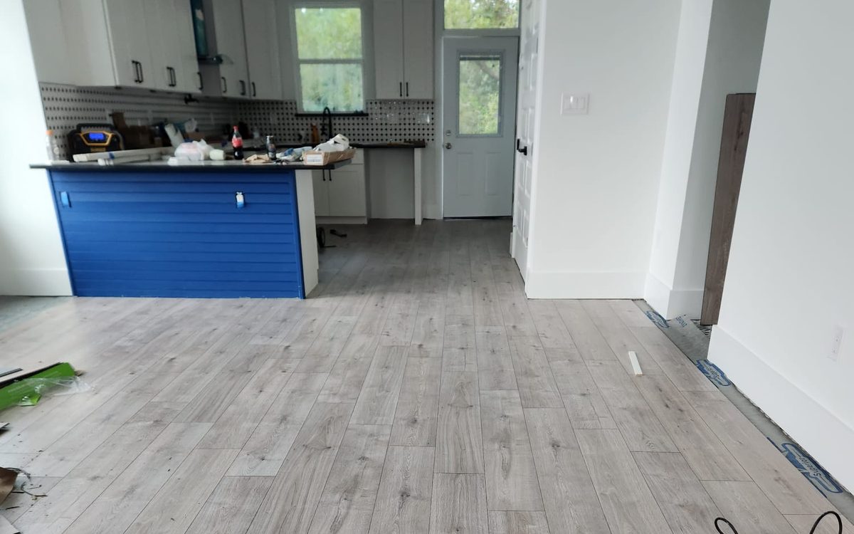 Kitchen with white shaker cabinets, patterned backsplash and a blue island, with new plank flooring