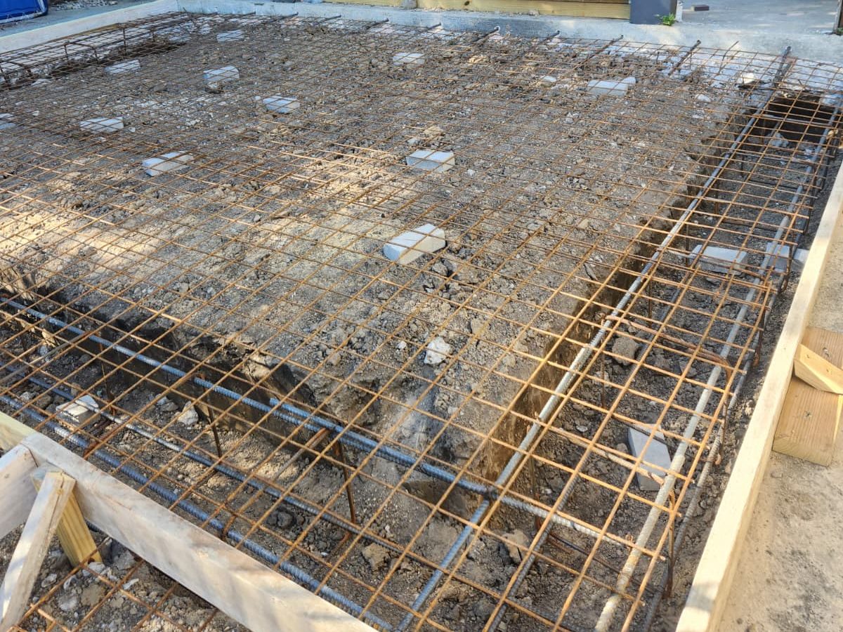 Wire mesh and rebar set over a gravel base for a concrete slab in front of a brick home