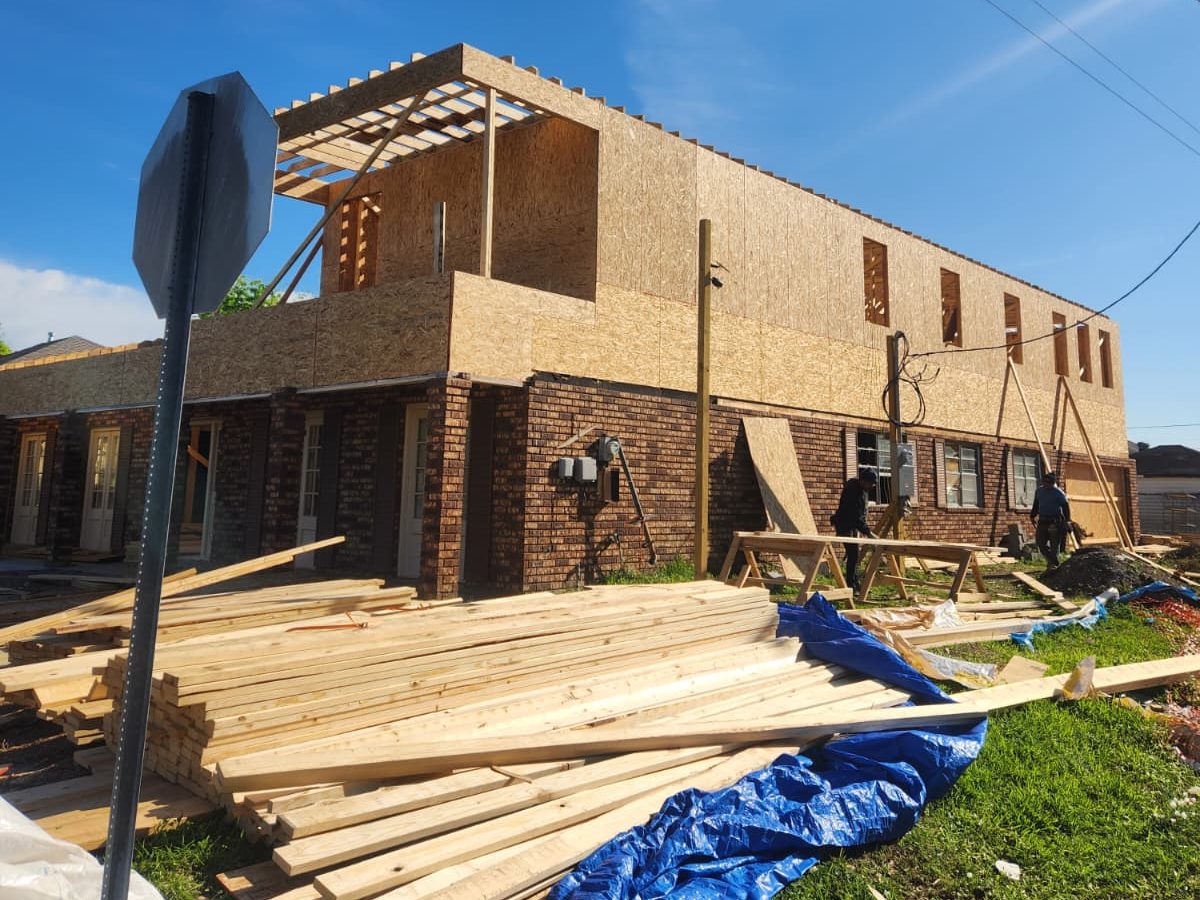 Crew building a second-story addition on a brick home, with lumber stacked in front