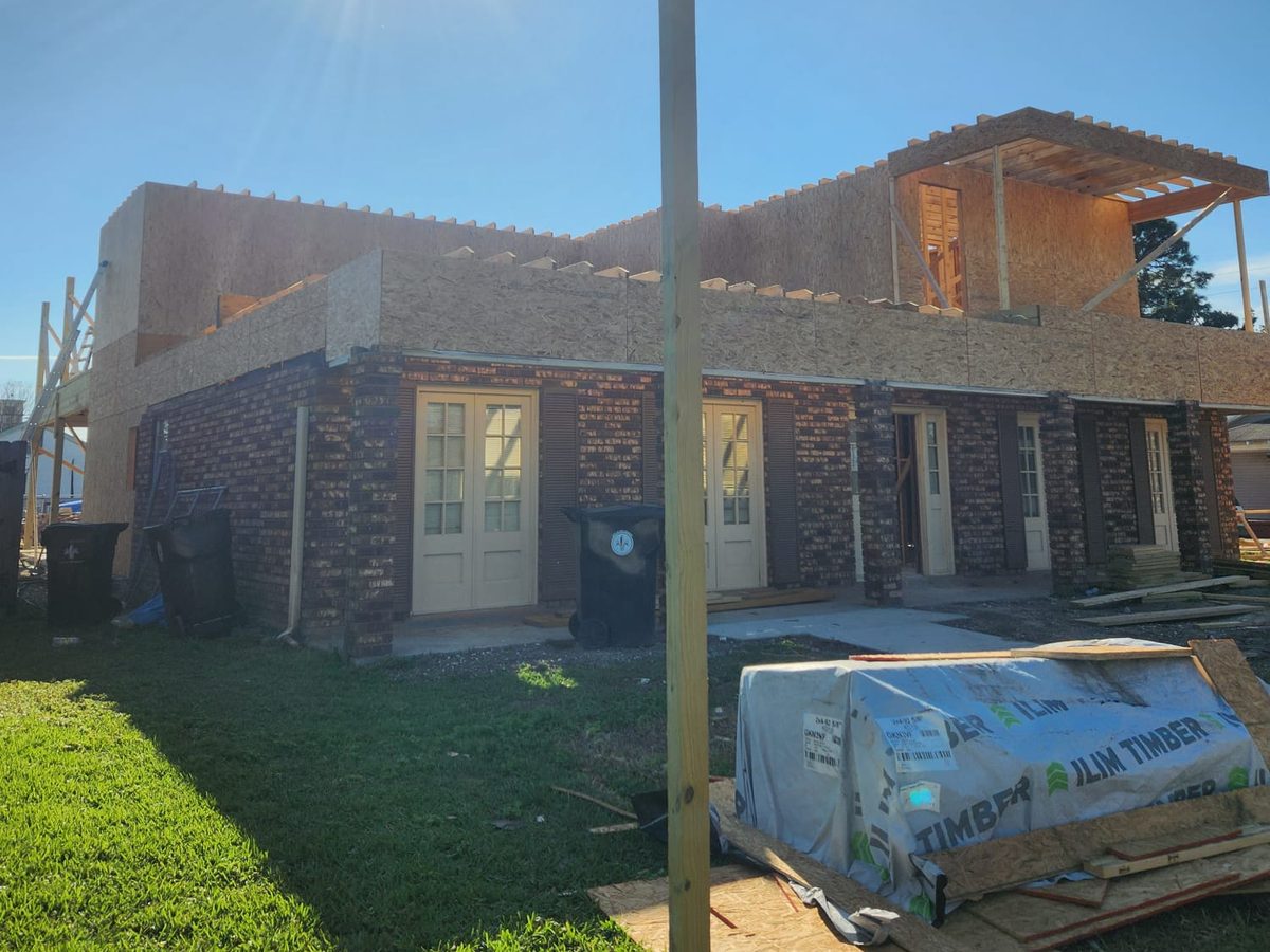 Brick home with a new upper story framed and sheathed, sun overhead