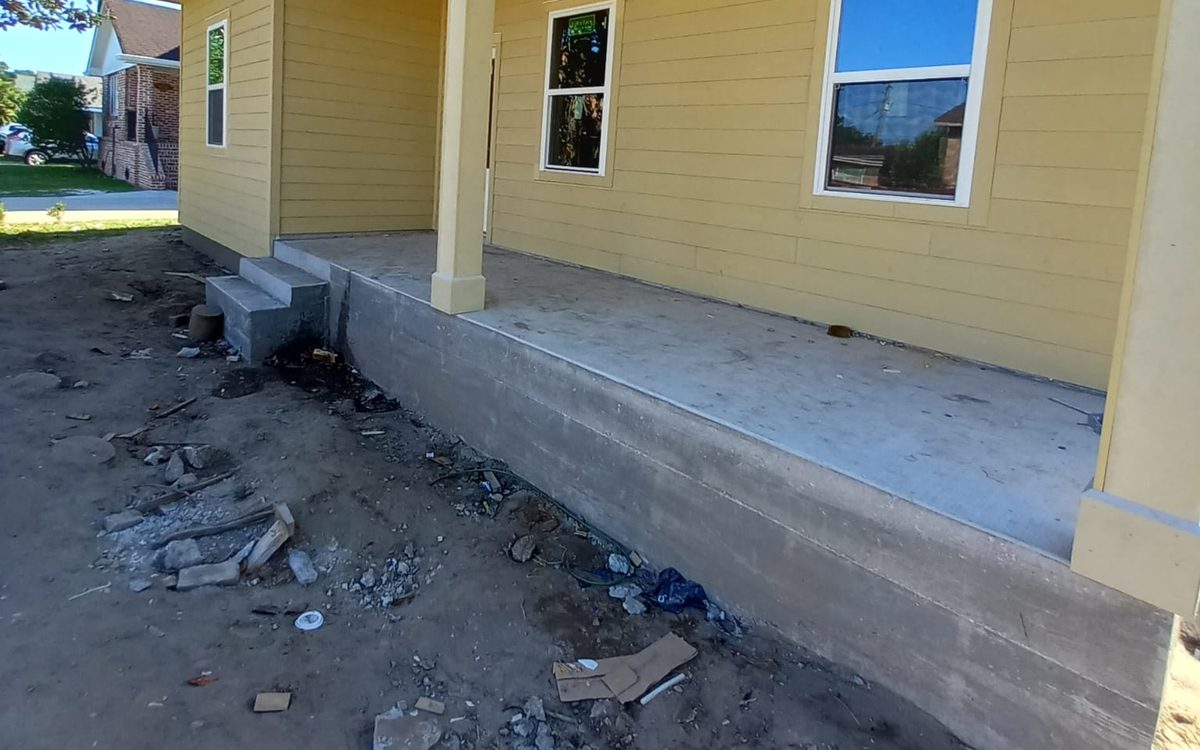 Long covered porch on a raised concrete base with yellow siding and new windows